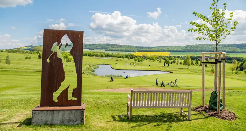 Die Corten-Stahl-Skulptur eines Golfers am ersten Abschlag, dahinter der Platz mit Teich.